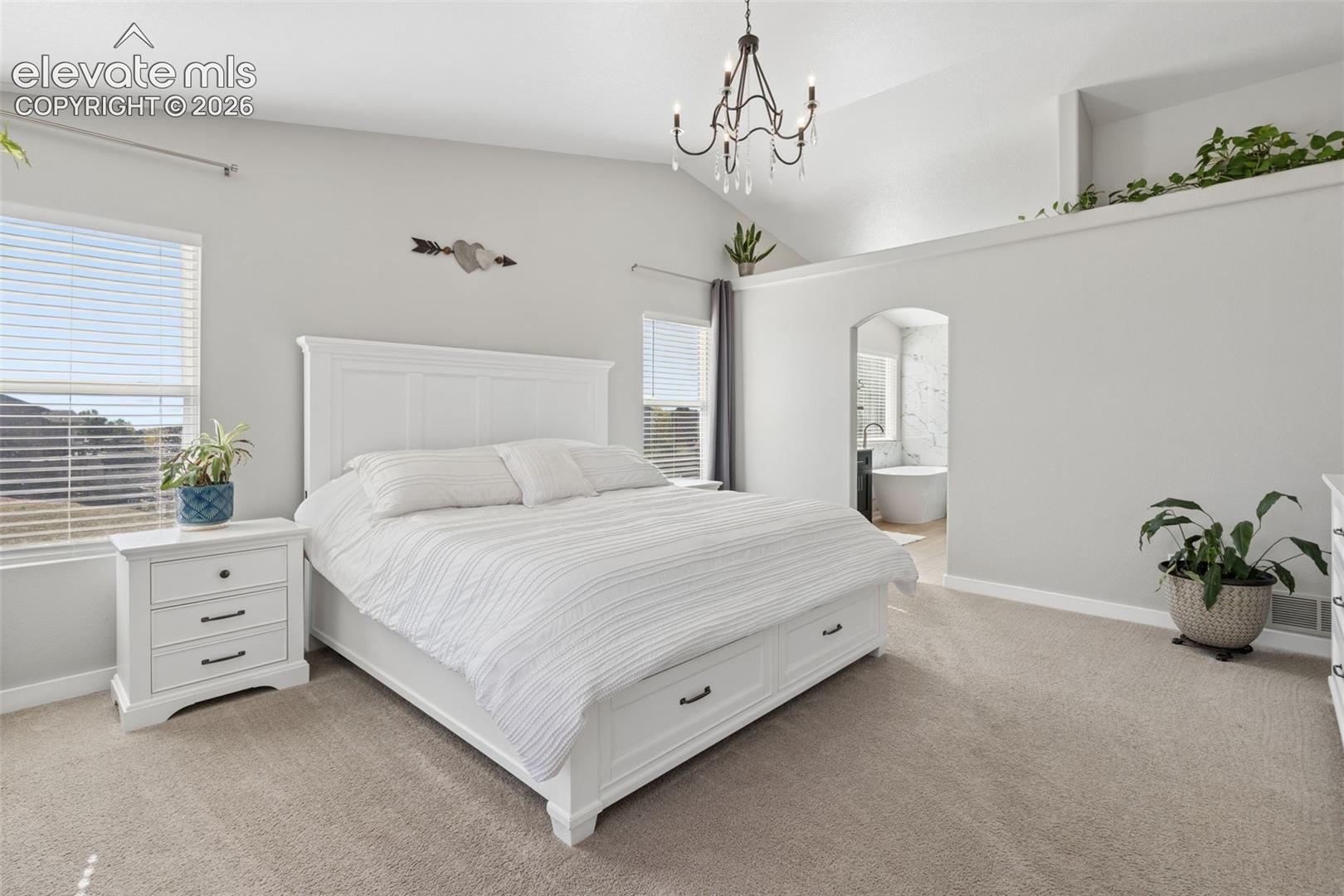 Vaulted ceiling with an attached chandelier, archway entry, interior ledge, and carpet flooring