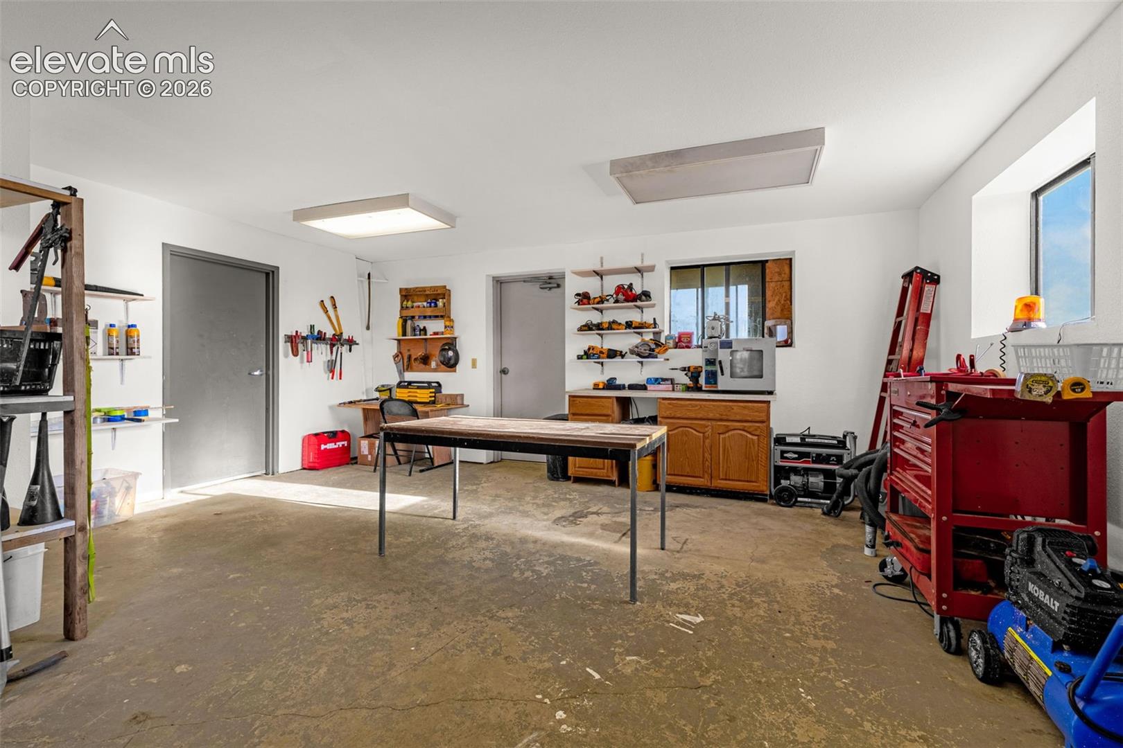 Spacious utility room with concrete flooring, multiple windows, built-in cabinetry, and overhead lighting