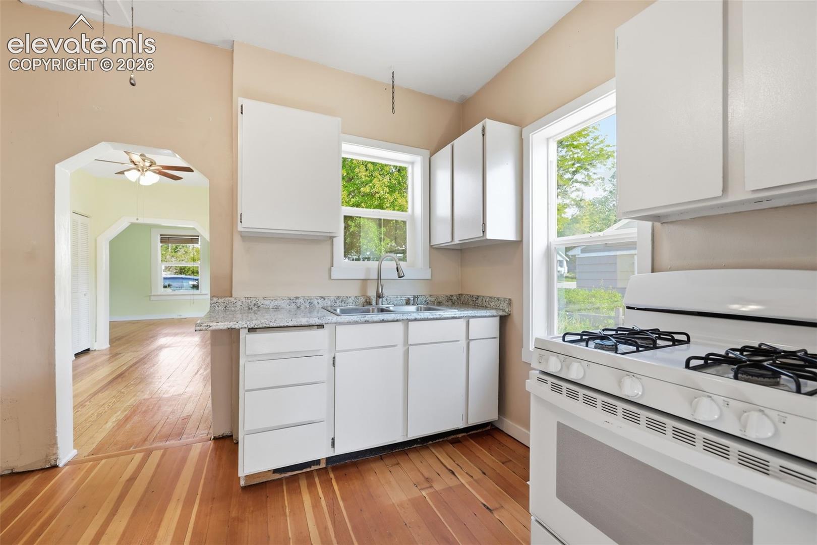 Kitchen featuring white cabinetry, a double basin sink, light-toned countertops, a white gas range, and pine hardwood flooring.