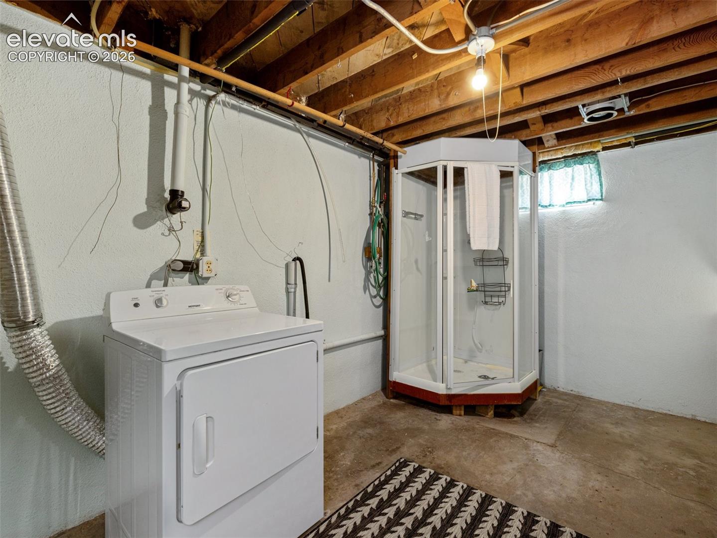 Utility space featuring concrete flooring, exposed wood joists, a standalone corner shower stall, and laundry connections