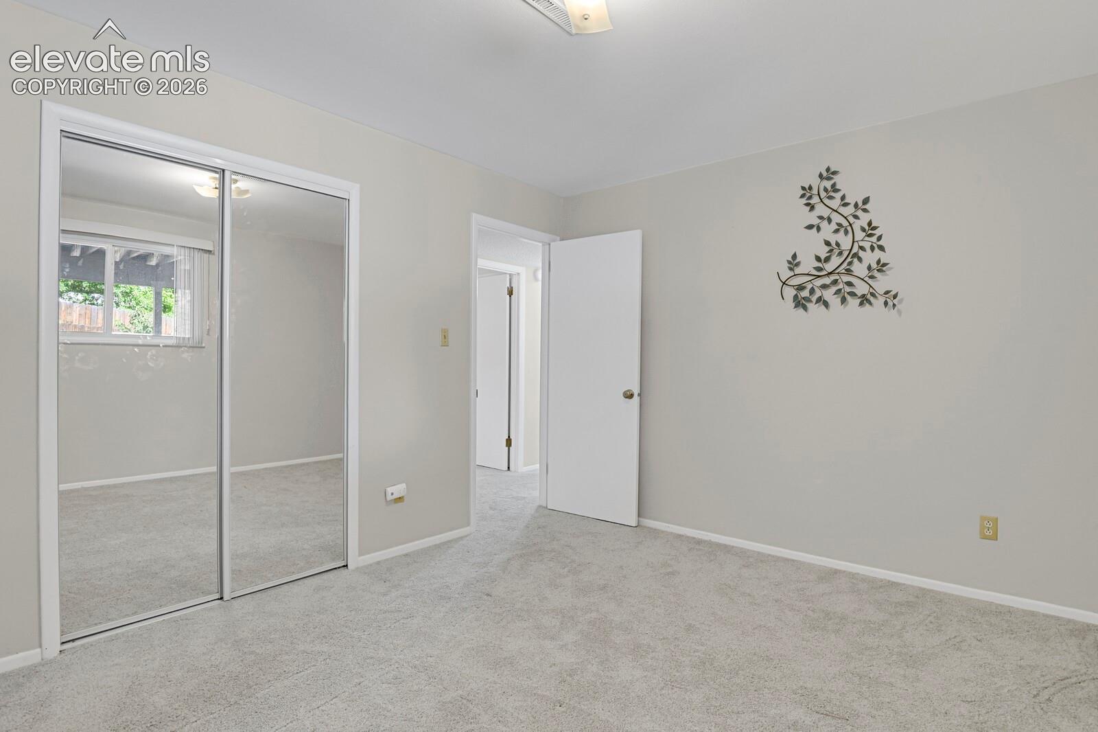 Spacious bedroom featuring neutral carpeting, mirrored sliding closet doors with white frame, white entry door, and soft overhead lighting