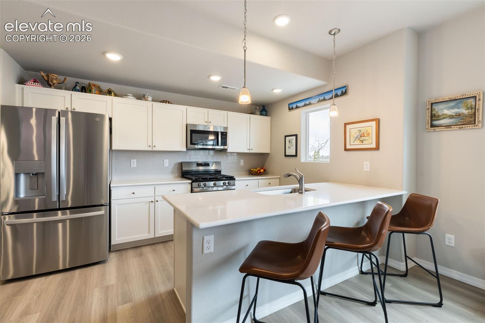 Modern kitchen featuring white shaker cabinetry, stainless steel appliances, a tile backsplash, and light-tone wood-finish flooring