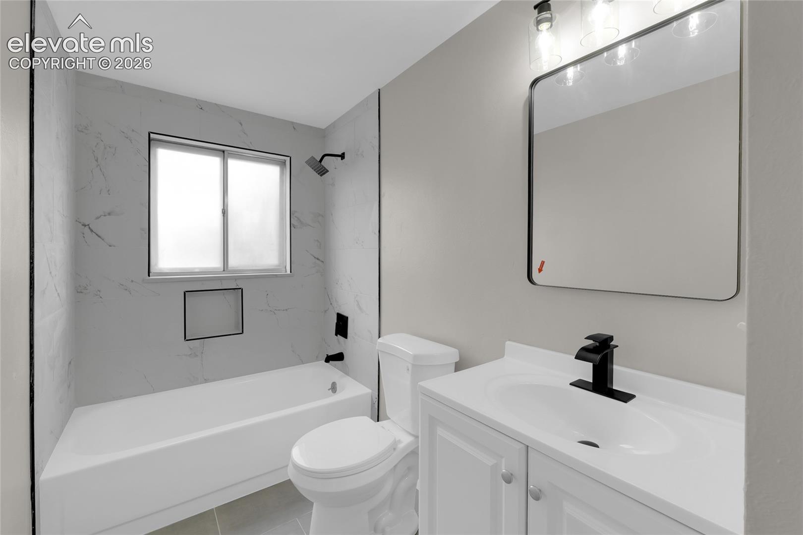 Modern bathroom featuring a white vanity with integrated sink, matte black fixtures, a rectangular framed mirror, and a tub with marble-look tile surround