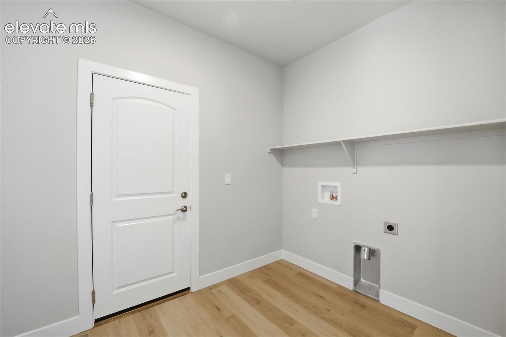 Utility space featuring wood-finish flooring, a solid-core interior door, a built-in wall shelf, and integrated water and ventilation hookups