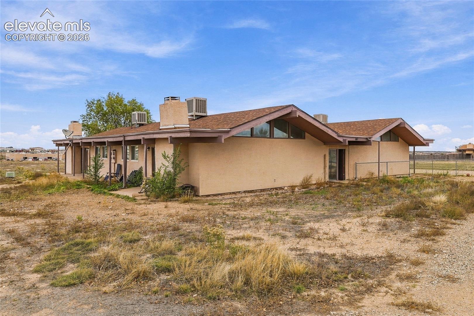 Single-story structure featuring a dual-gabled roofline, stucco exterior, clerestory windows, and covered patio area