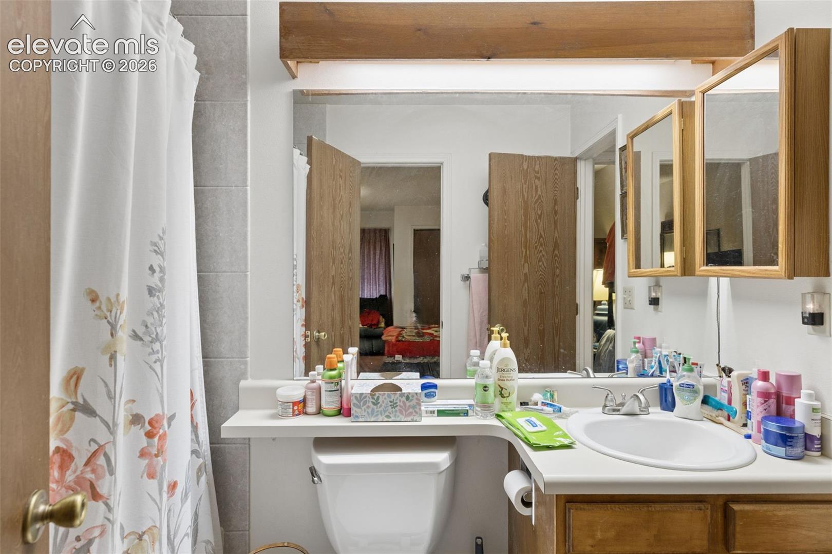 Bathroom vanity featuring a solid-surface integrated sink and countertop, wood-finish cabinetry, and a tri-fold wooden medicine cabinet with integrated wood valance lighting