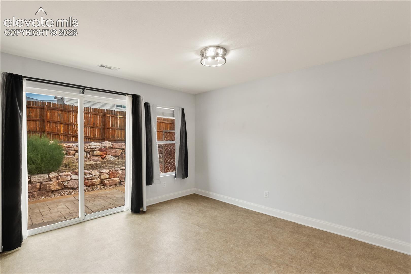 Interior featuring sliding glass doors with exterior access to a stone-paved patio, a multi-tiered rock retaining wall, a wood privacy fence, and a ceiling-mounted light fixture