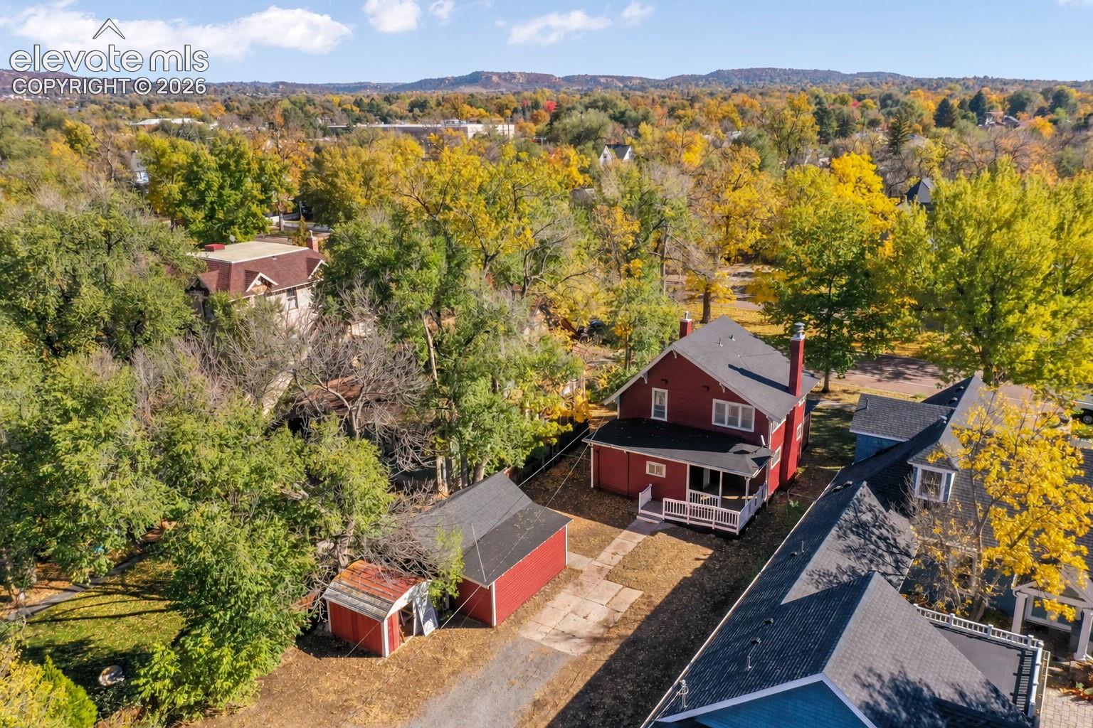 Two-story residence featuring a covered deck, detached garage, and mature tree canopy, set against a mountain backdrop