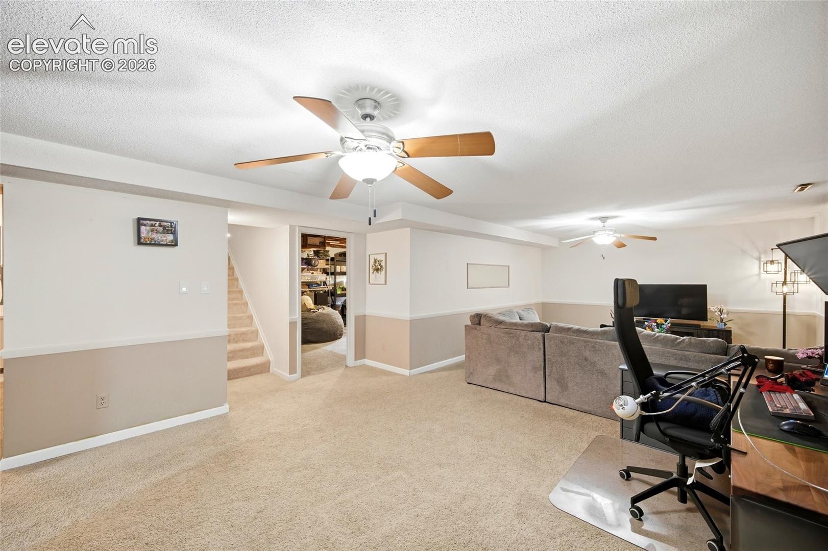 Neutral-toned interior featuring wall-to-wall carpeting, two ceiling fans with integrated lighting, and painted wainscoting
