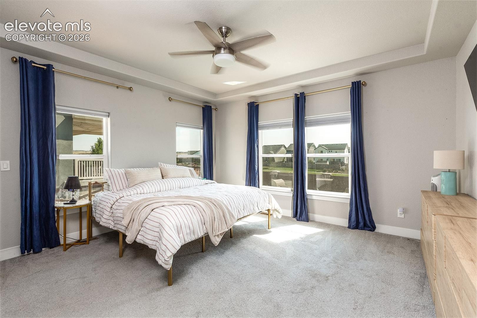 Recessed ceiling with ceiling fan, light-toned carpeting, multiple windows, and a built-in wall-mounted television