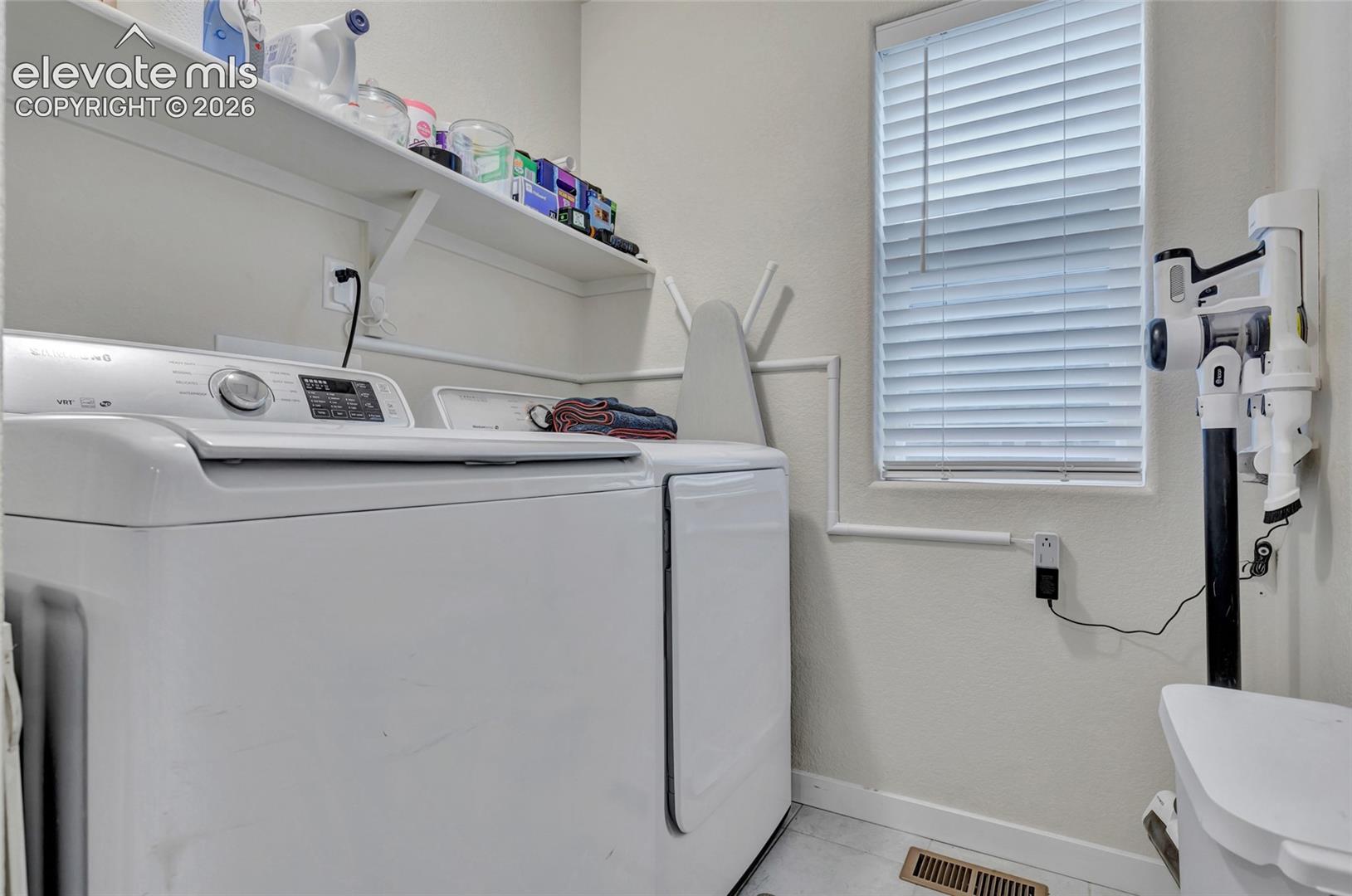 Laundry room featuring a front-load washer and dryer pair, floating shelving with storage capacity, louvered window with natural light, and tile flooring