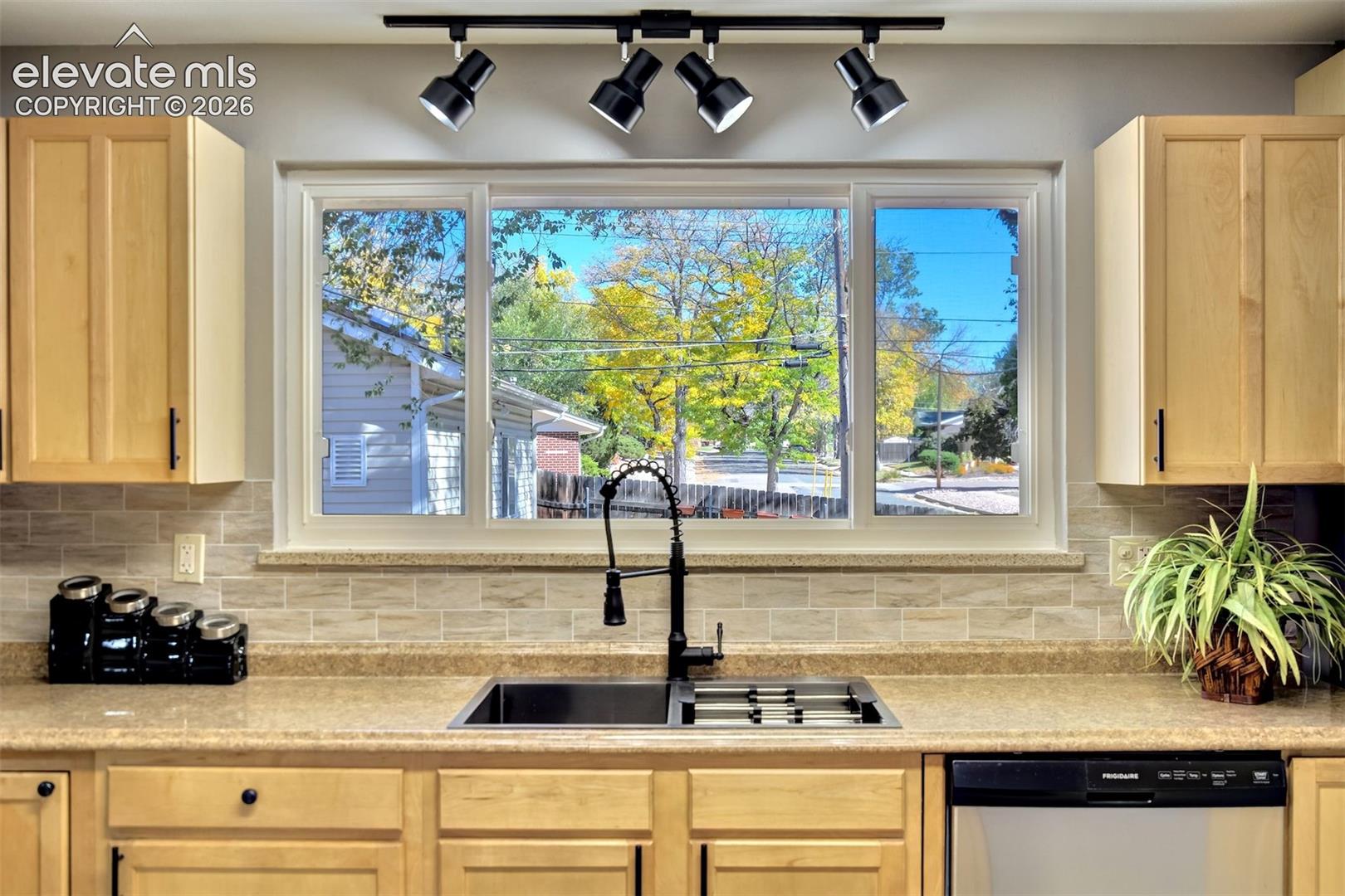 Kitchen featuring light-finish cabinetry, neutral stone-composite countertop, subway tile backsplash, stainless steel dual-basin undermount sink with a matte black pull-down faucet, and adjustable four-light track lighting