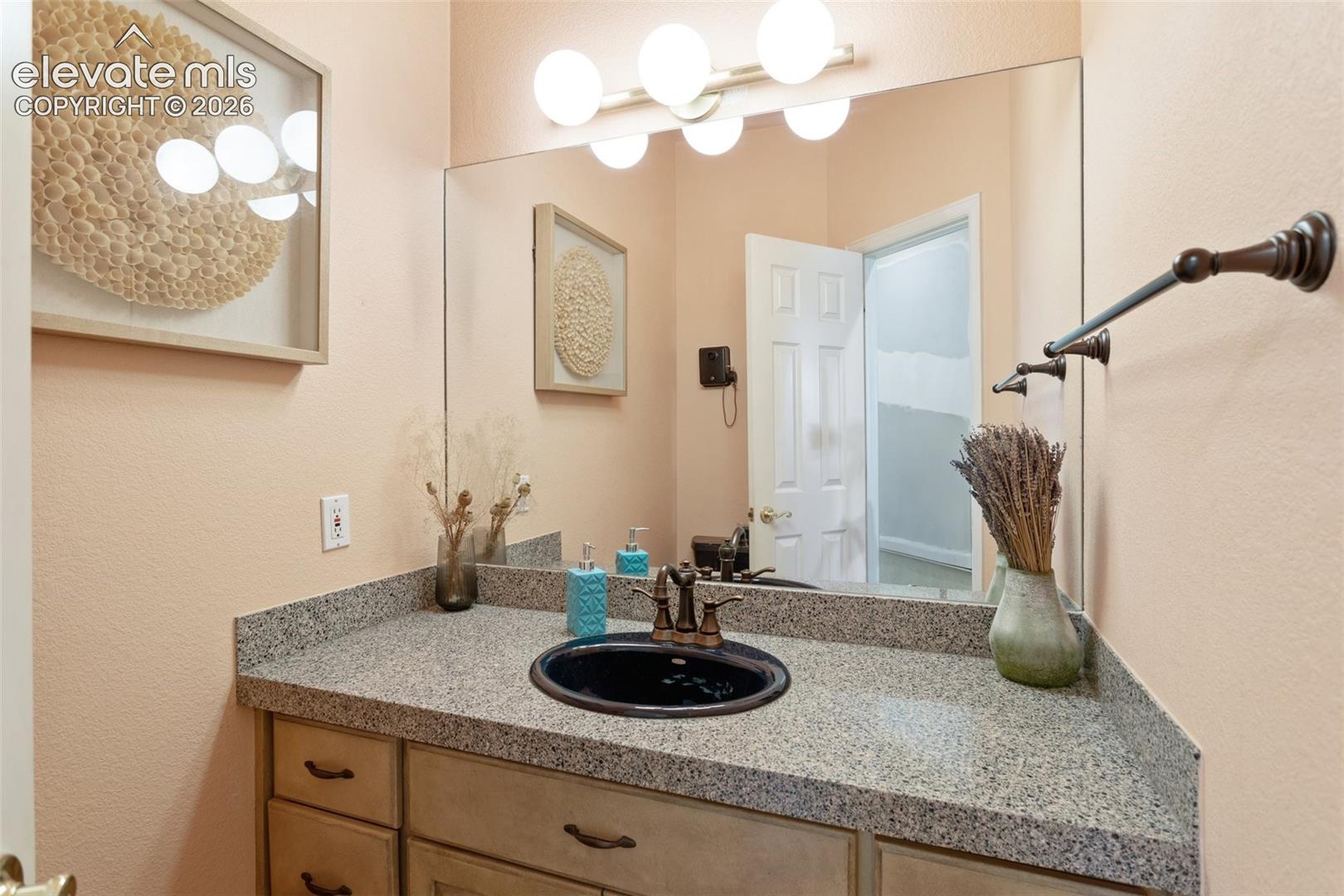 Bathroom vanity featuring a speckled countertop, a black oval sink, and a bronze-finish faucet