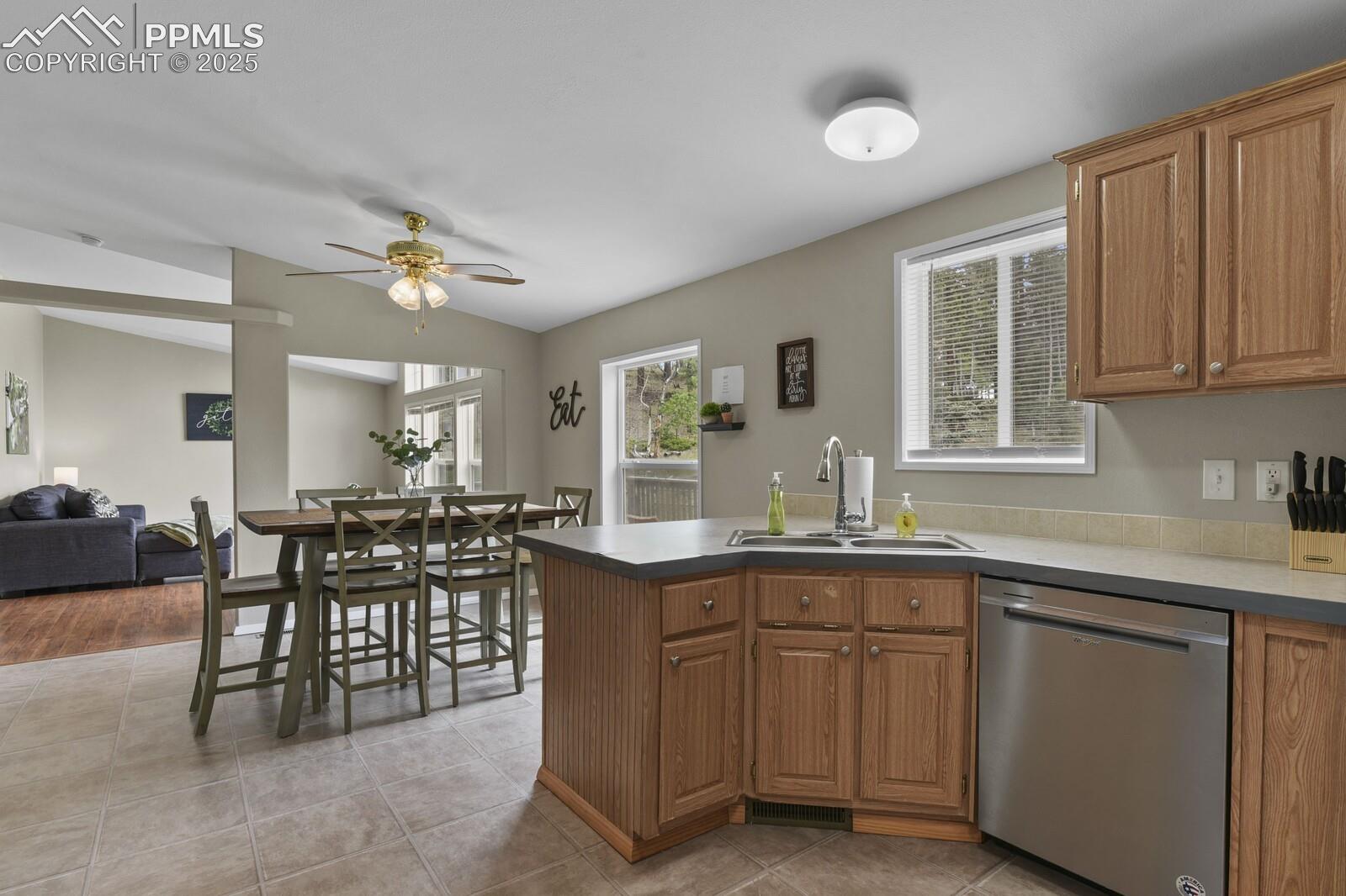 Kitchen featuring dishwasher, a peninsula, brown cabinetry, light tile patterned floors, and lofted ceiling