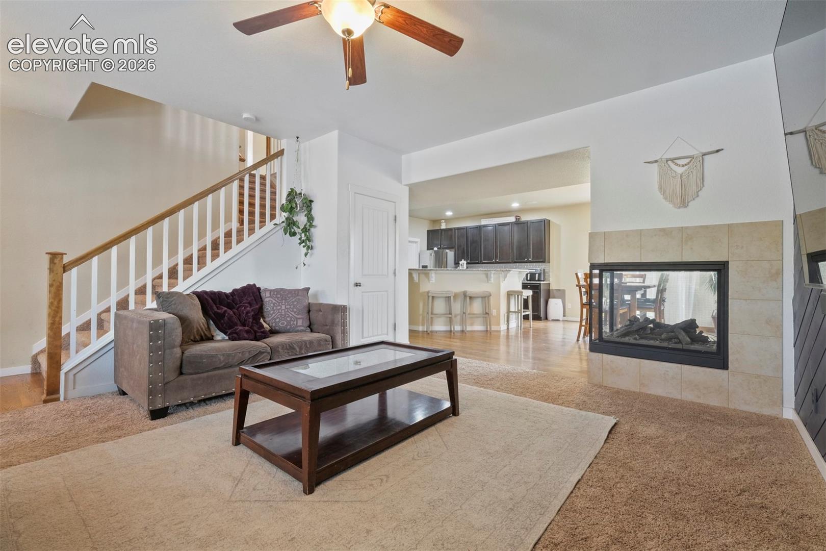 Main Level: Open-concept living space featuring a tiled fireplace with an integrated firebox, wood-finish flooring, a ceiling fan, and staircase with wood handrails