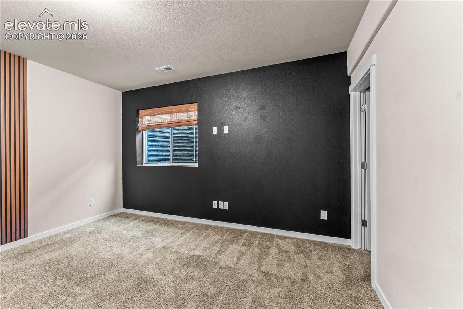 Bedroom interior featuring wall-to-wall carpeting, a monochromatic accent wall, vertical wood-slat wall paneling, and an egress window with a window well