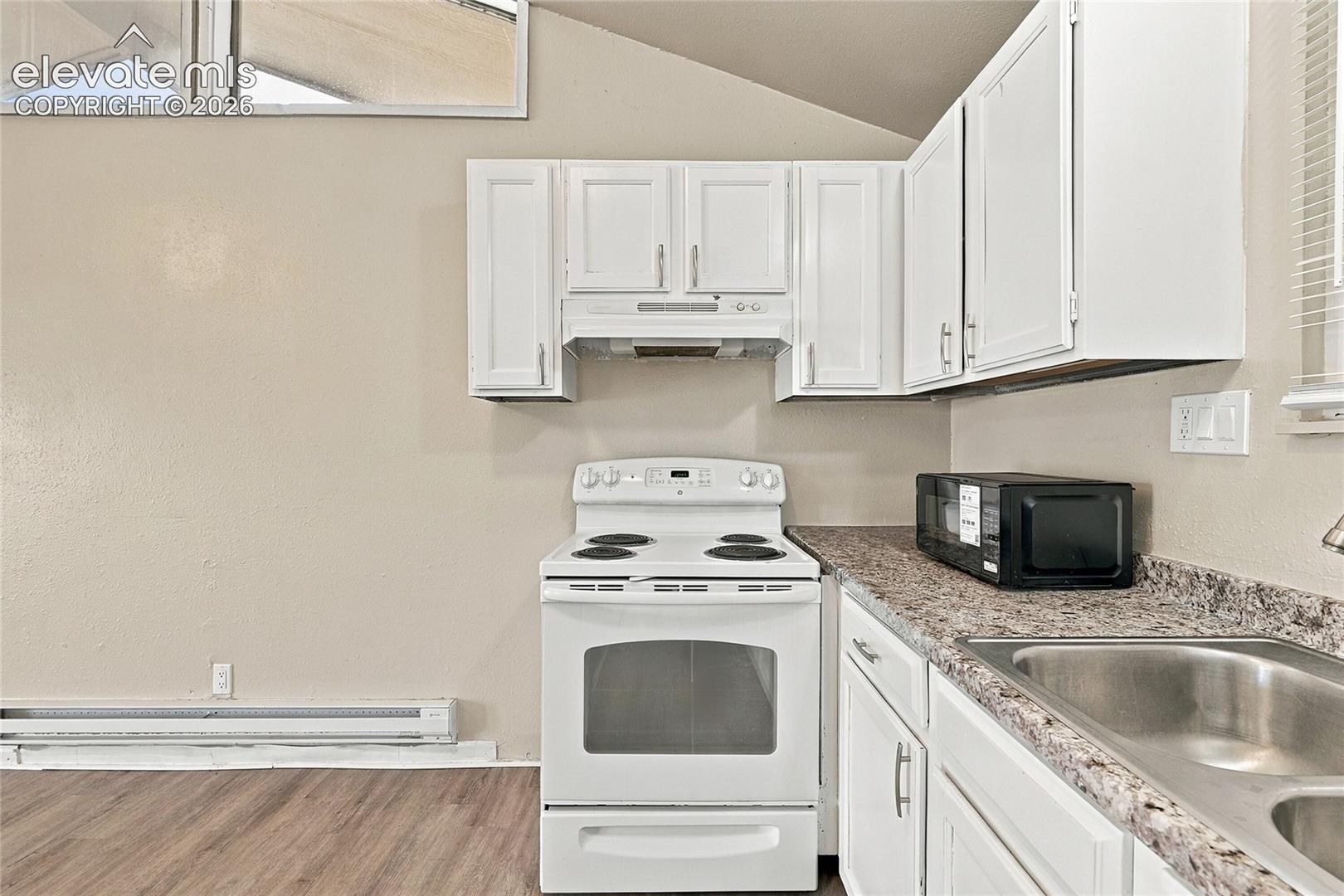 Kitchen featuring white cabinetry, wood-finish flooring, stone-patterned laminate countertops, and a stainless steel double-basin sink under a vaulted ceiling