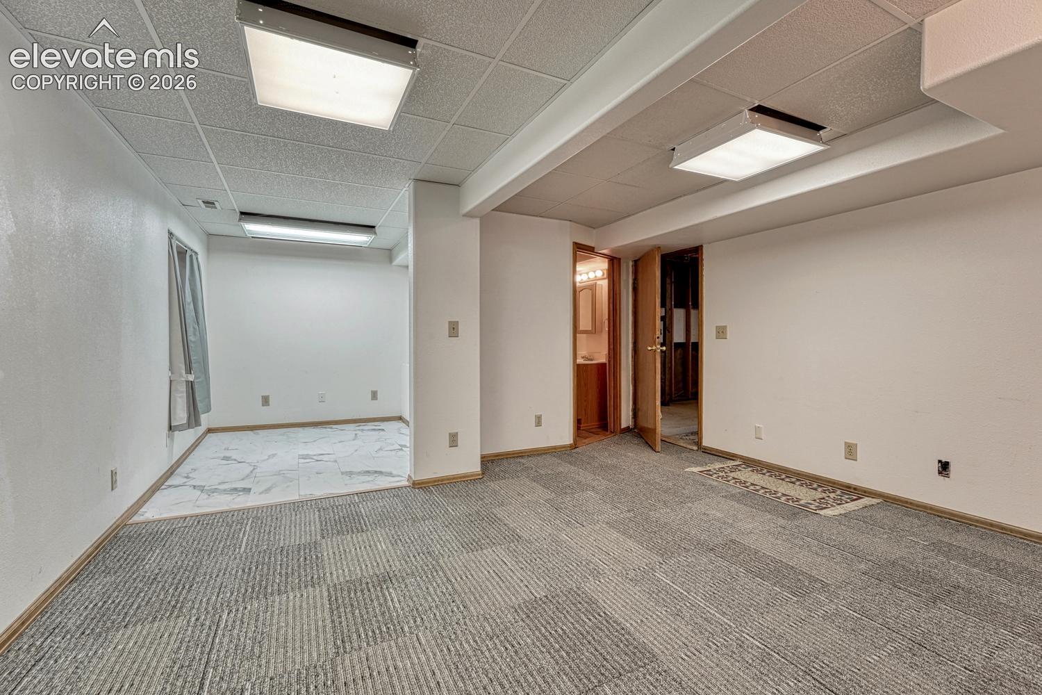 Recessed drop ceiling, overhead fluorescent lighting, wood-finish trim, patterned carpet flooring, and white wall finishes