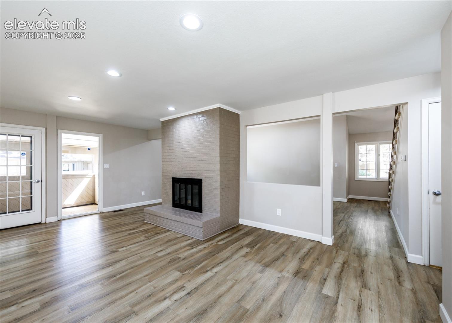 Living area featuring wood-finish flooring, recessed lighting, a brick fireplace with a hearth, and a glass-paneled exterior door