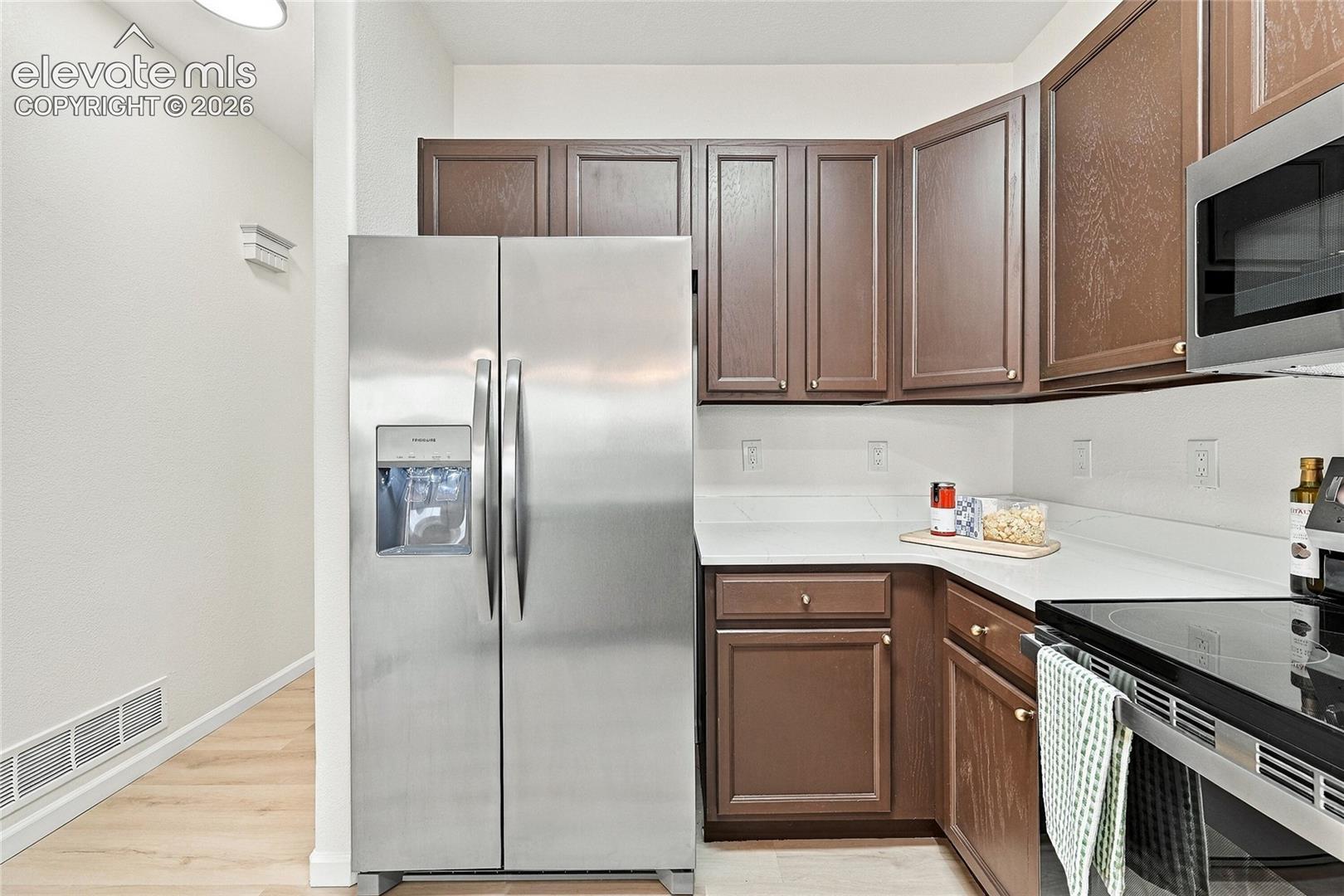 Kitchen featuring dark wood cabinetry, solid-surface countertops, and stainless steel appliances including a refrigerator and microwave