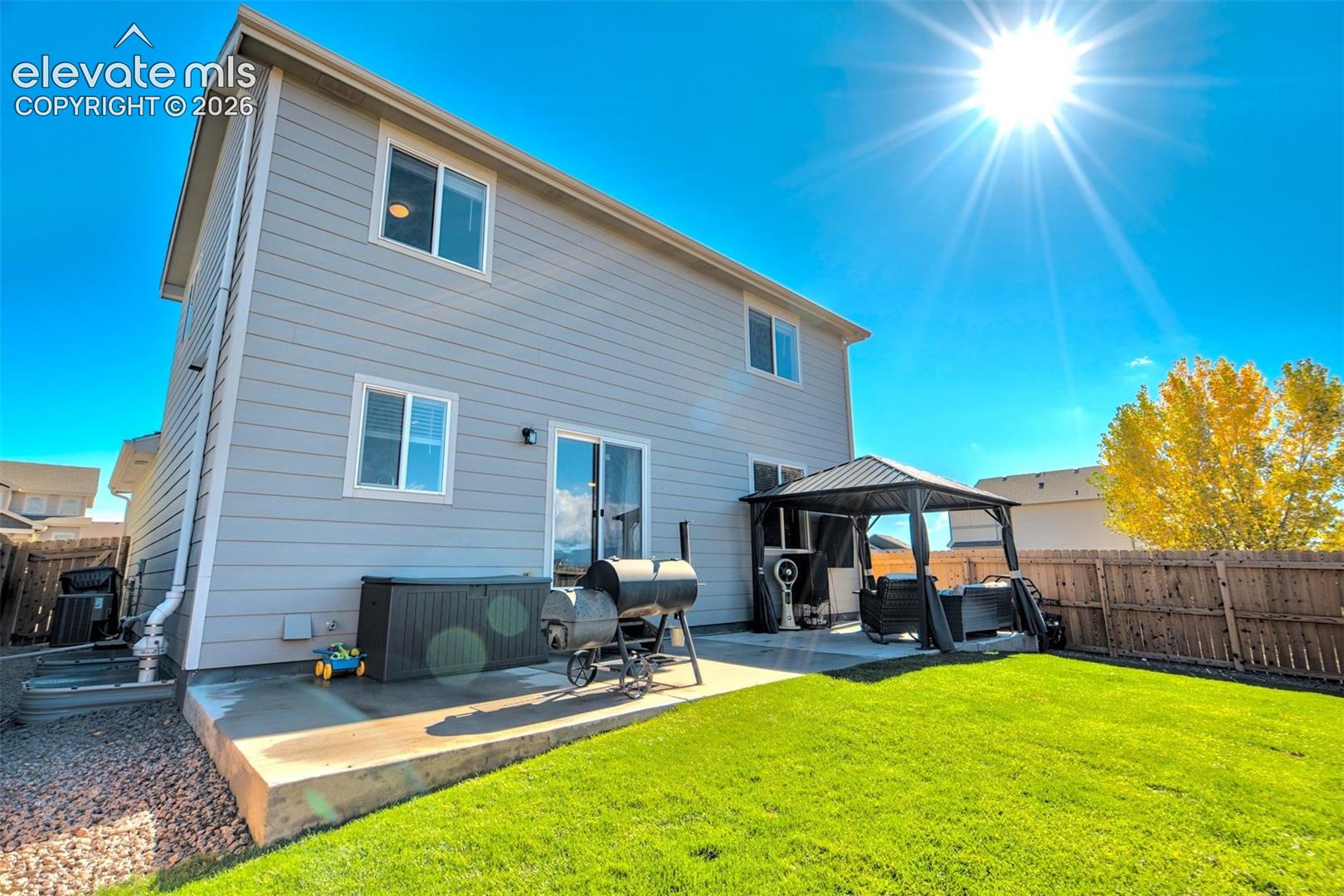 Two-story residence featuring light-toned horizontal siding, a concrete rear patio, and a fully fenced backyard with a lawn
