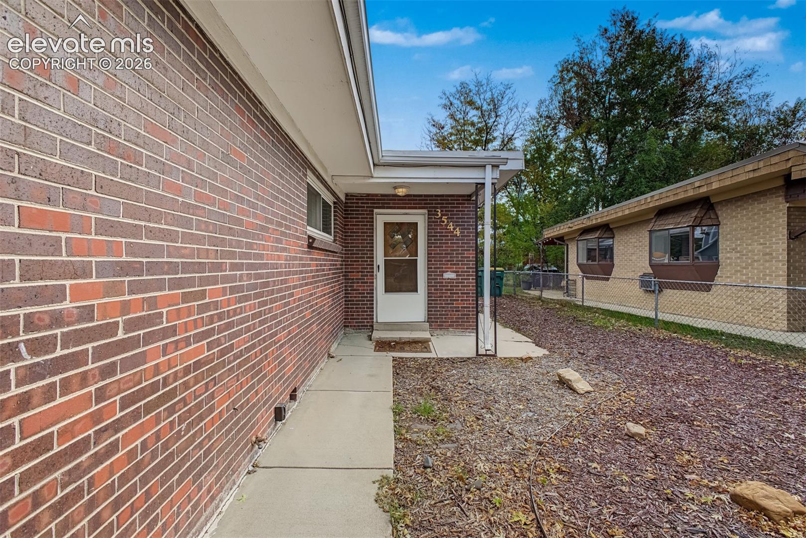 Red brick exterior featuring a covered entryway, concrete sidewalk, and metal support post