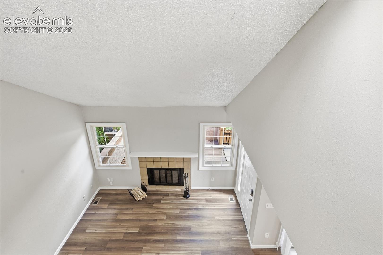 Living area featuring wood-finish flooring, a fireplace with a brick surround and mantel, and multiple windows