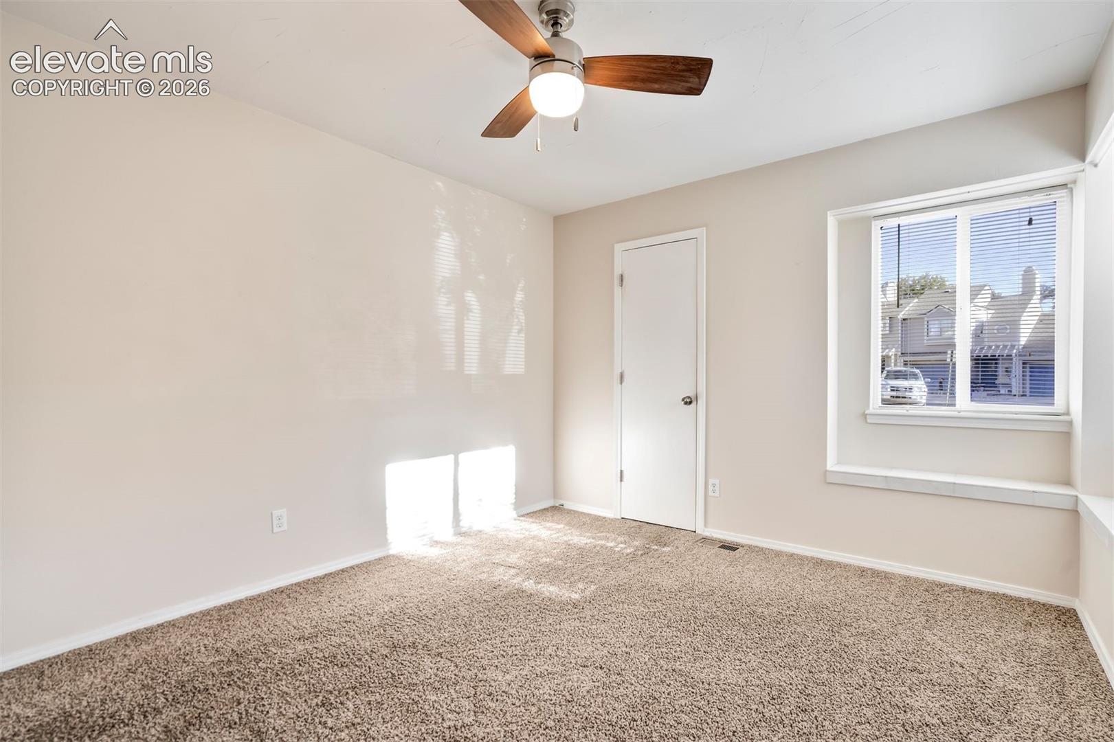 Neutral-toned interior room featuring wall-to-wall carpeting, a multi-pane window with a deep sill, and a ceiling-mounted light fixture with a three-blade fan