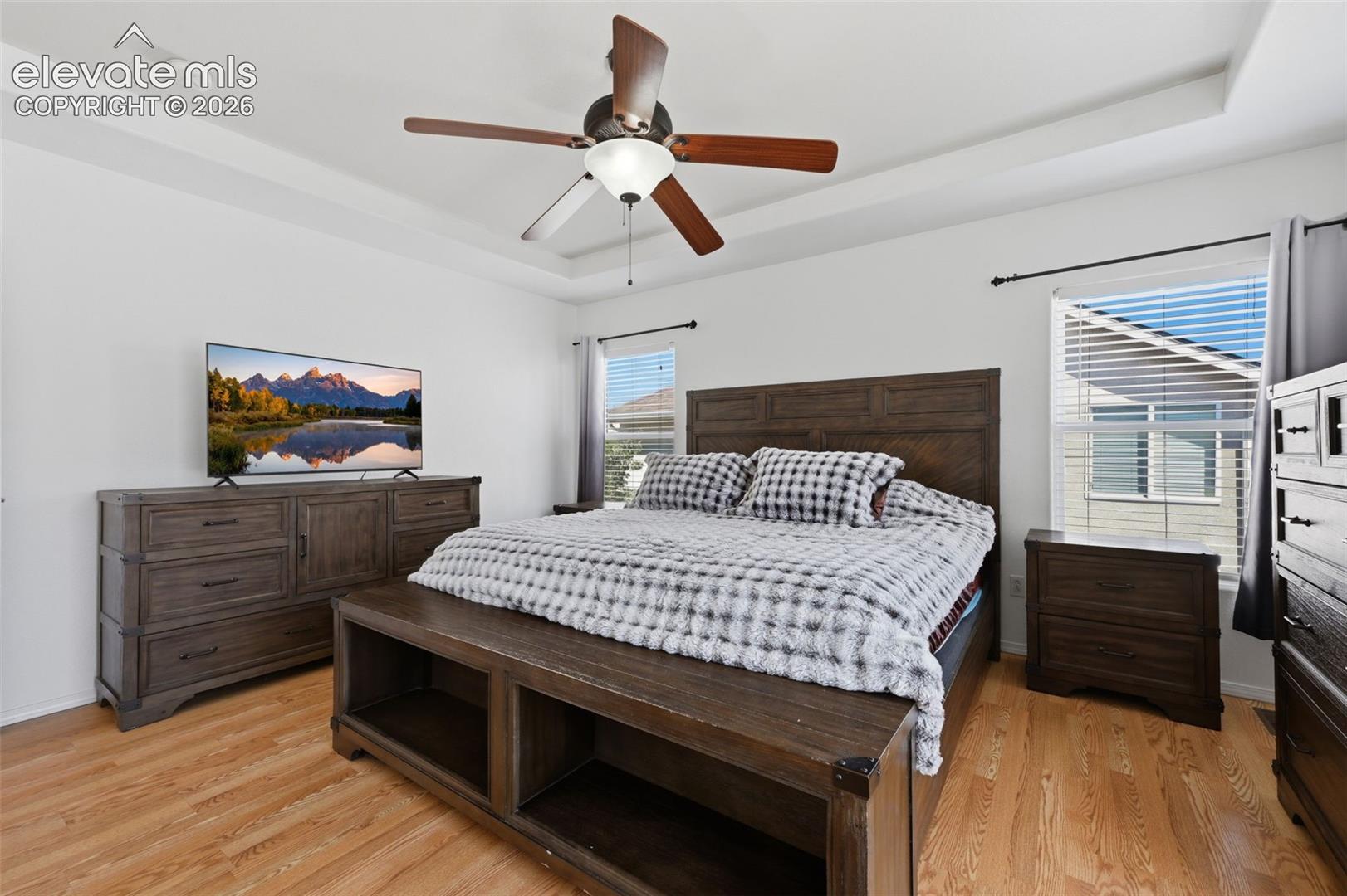 Tray ceiling with a ceiling fan, wood-finish flooring, and white walls