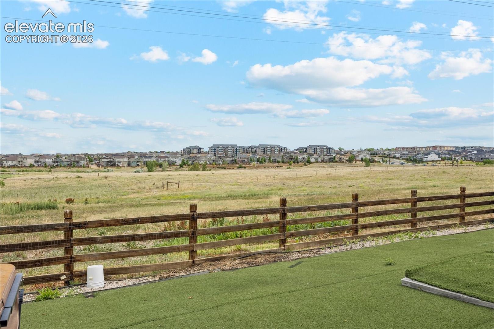 Expansive outdoor space featuring artificial turf, a rustic wooden fence, and open field vistas