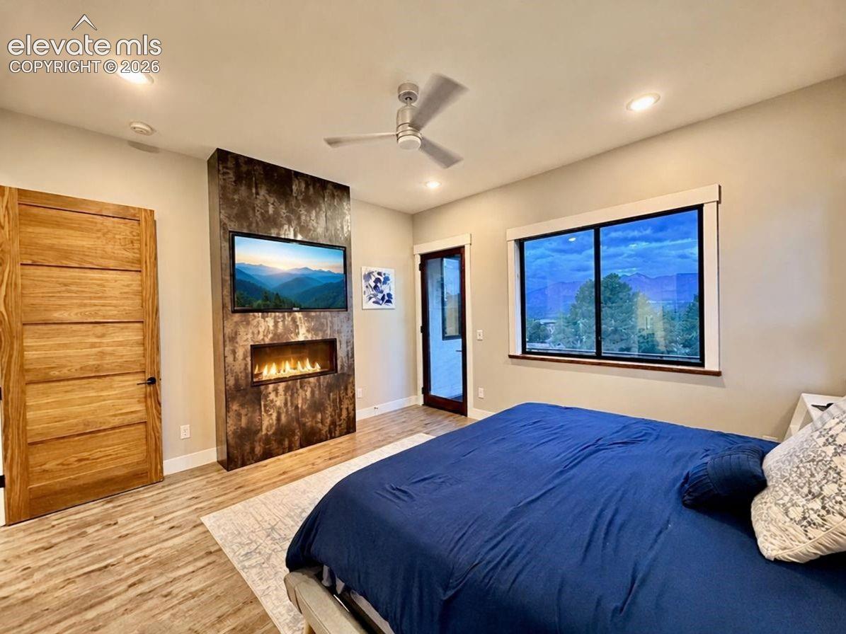 Wood-finish flooring, accent wall with linear fireplace, recessed lighting, ceiling fan, and large window