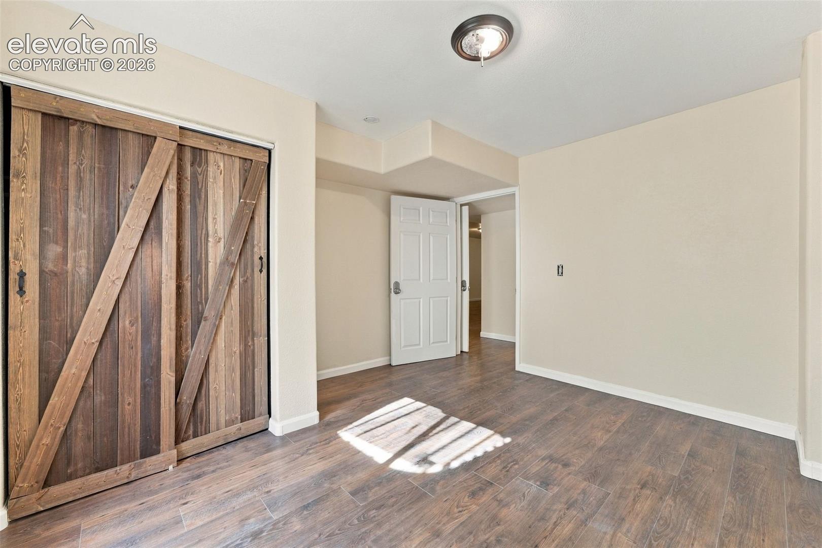 Room featuring wood-finish flooring, sliding barn-style door with rustic hardware, and neutral wall paint