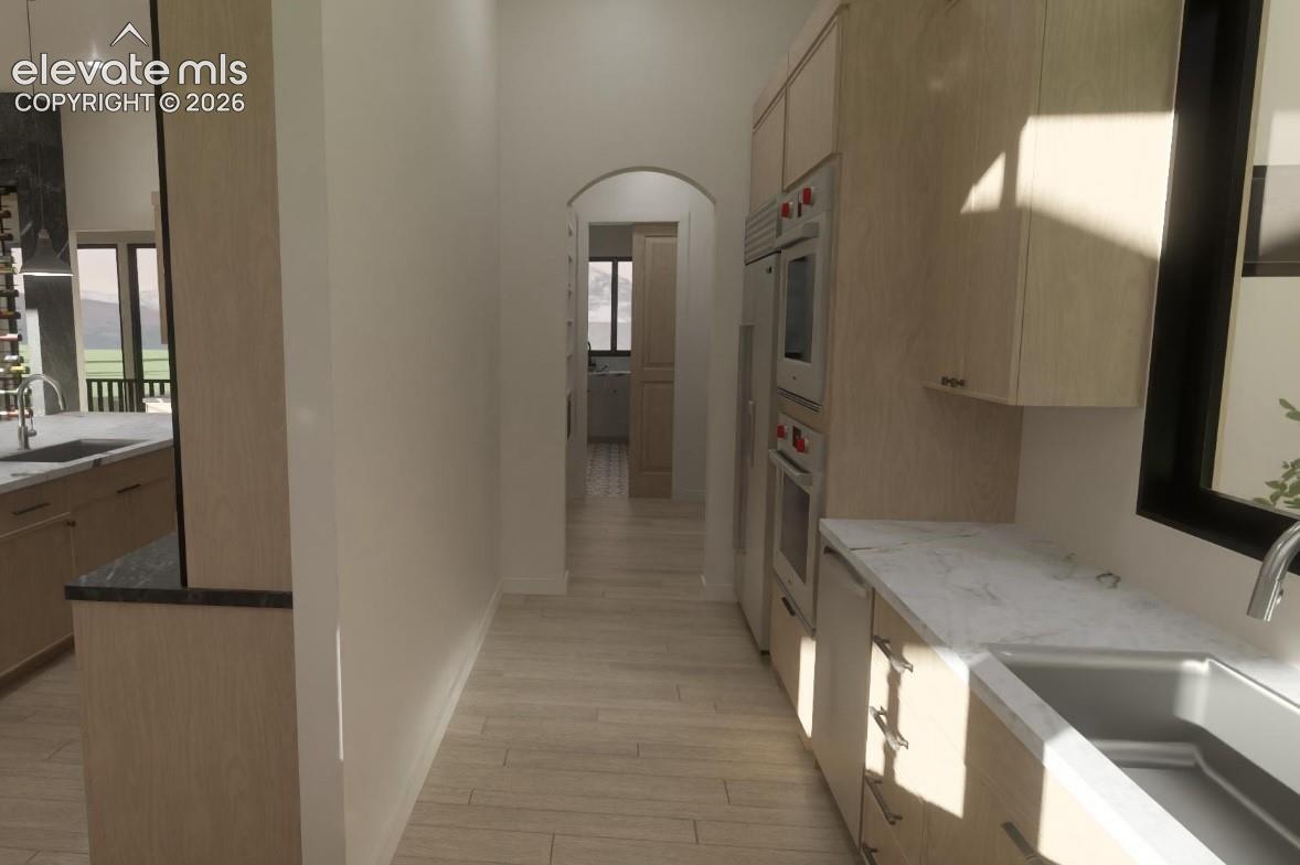 Secondary prep kitchen and separate food pantry with light wood-finish cabinetry, stainless steel appliances, light-toned wood-finish flooring, and white countertops