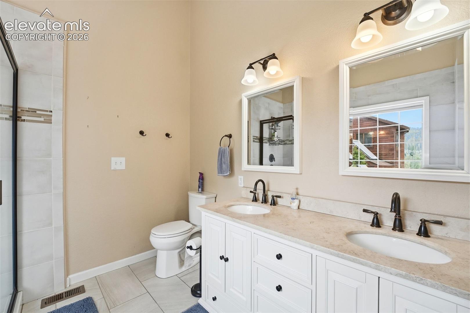 Bathroom featuring a double vanity with white cabinetry, light-toned countertops, two framed mirrors, and individual light fixtures