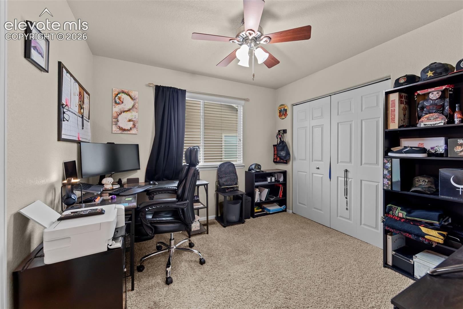 Neutral-toned walls, textured carpeting, window with horizontal blinds, and a ceiling fan with light fixture