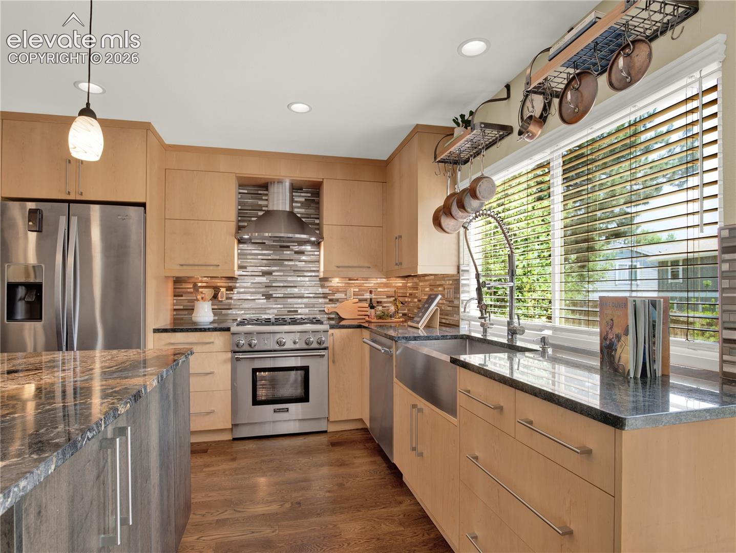 Kitchen featuring light wood flat-panel cabinetry, dark stone countertops, stainless steel farmhouse sink, professional-grade gas range with stainless steel hood, and multicolored mosaic tile backsplash