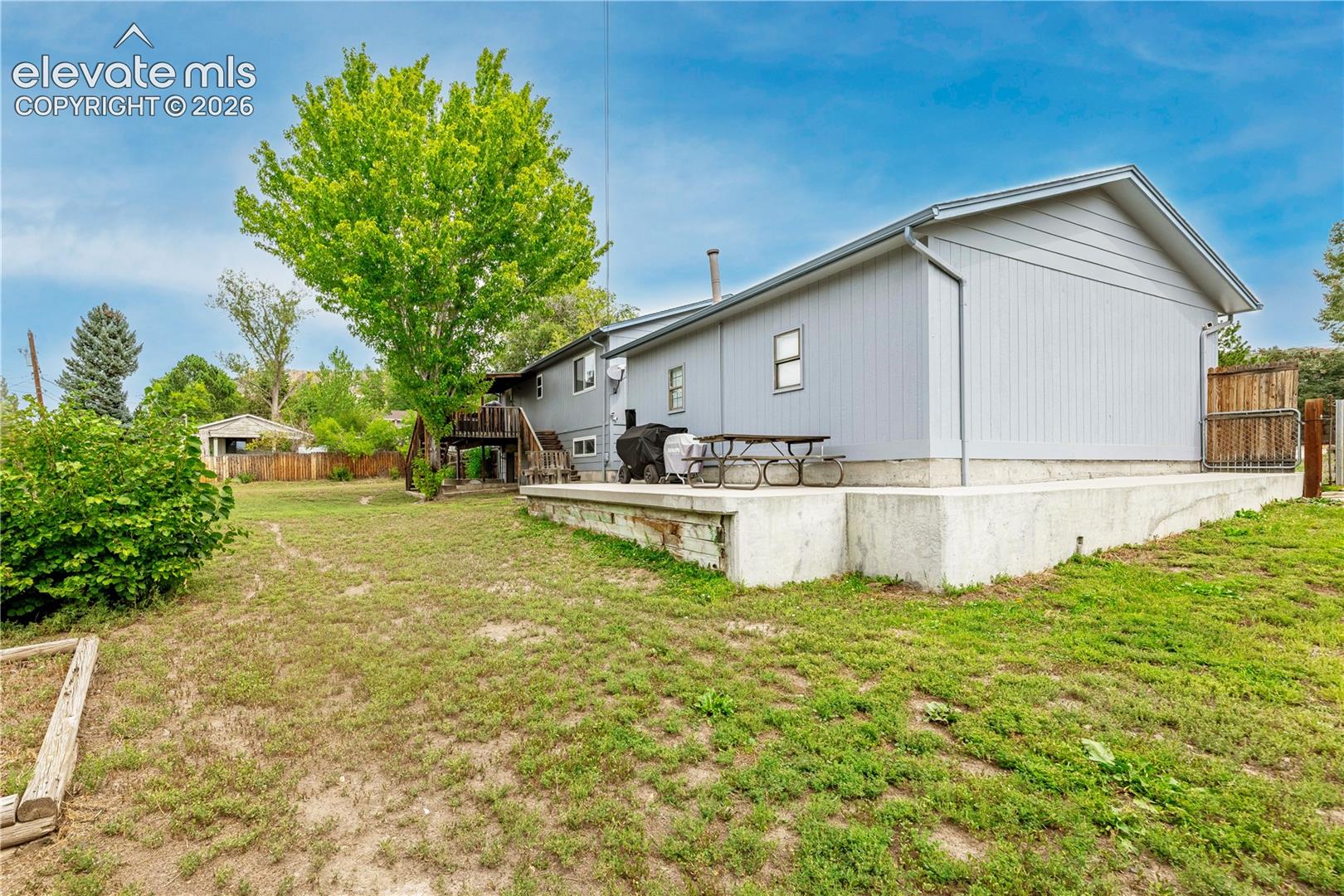 Exterior siding, concrete patio, and raised wood deck on a generous lot with mature trees