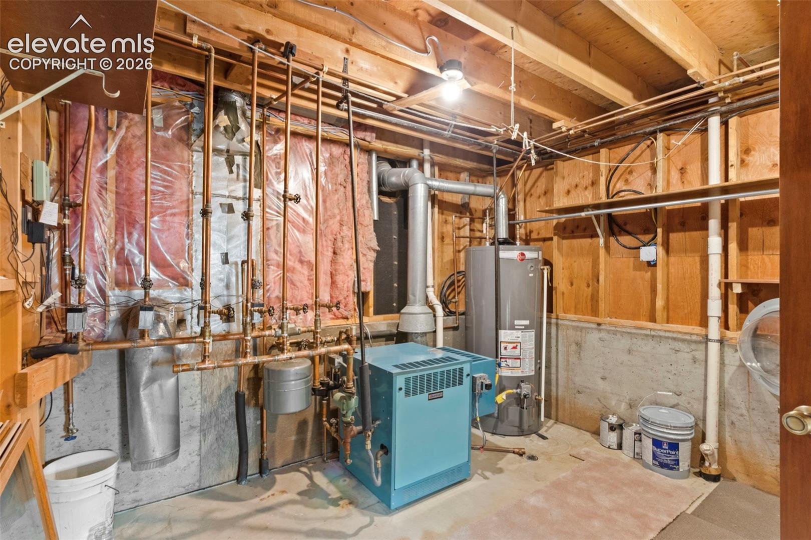 Utility space featuring a boiler, a vertical hot water tank, exposed copper plumbing infrastructure, and concrete foundation walls