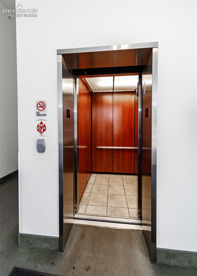 Elevator featuring stainless steel framing, wood-finish interior paneling, tile flooring, and a mounted metal handrail