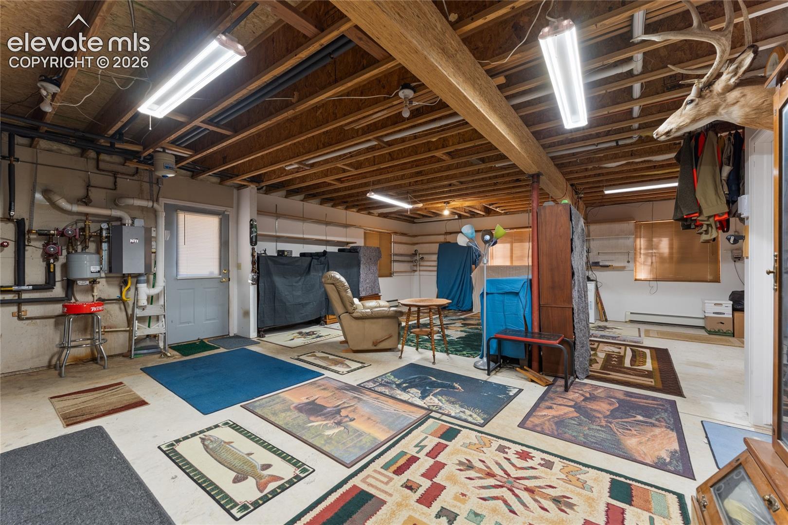 Spacious unfinished basement offering exposed wooden ceiling joists, concrete flooring, and multiple ceiling-mounted fluorescent light fixtures
