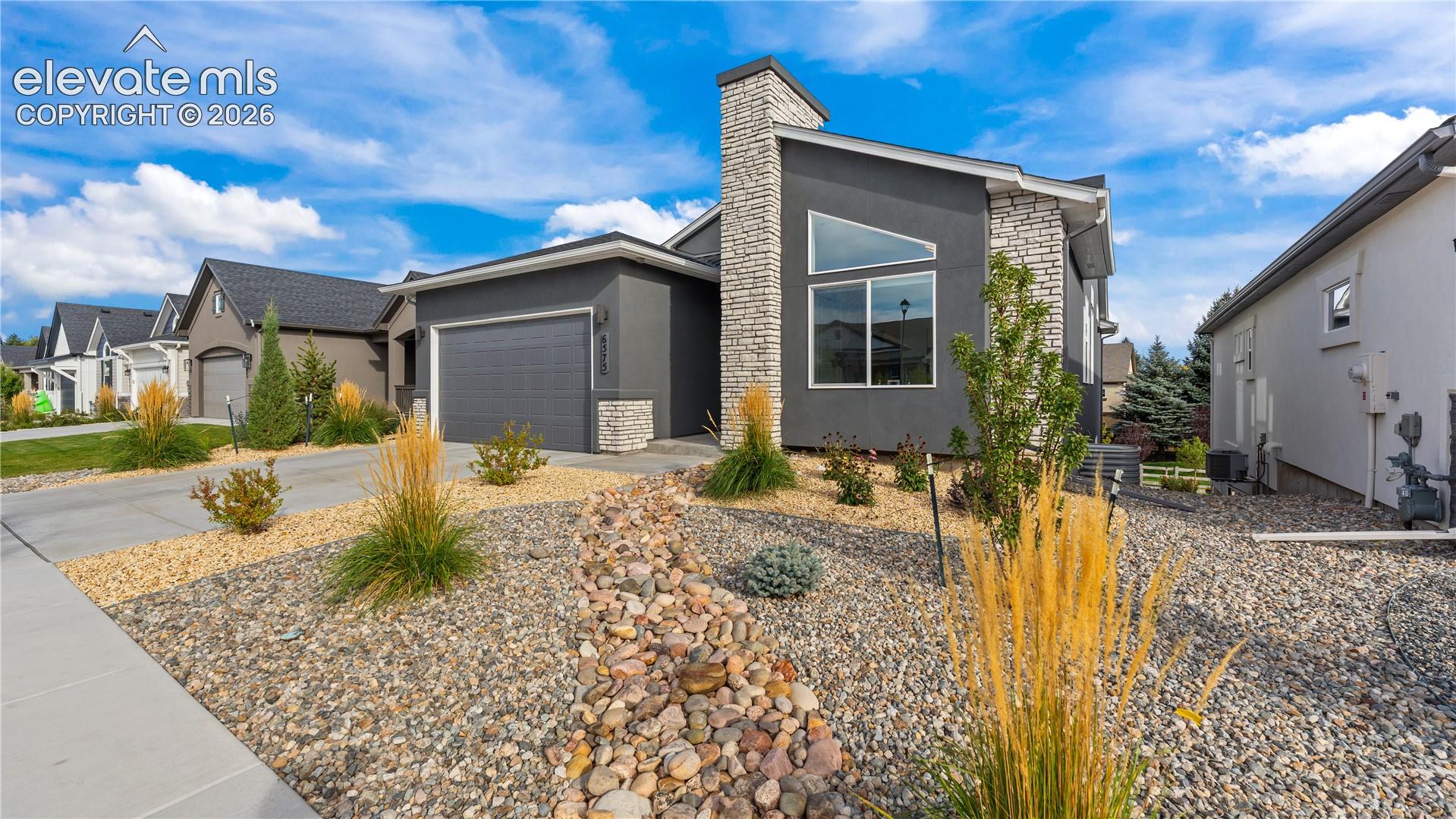 Contemporary exterior featuring a stone-clad chimney, angular roofline, two-tone finish, integrated garage, and xeriscaped front yard