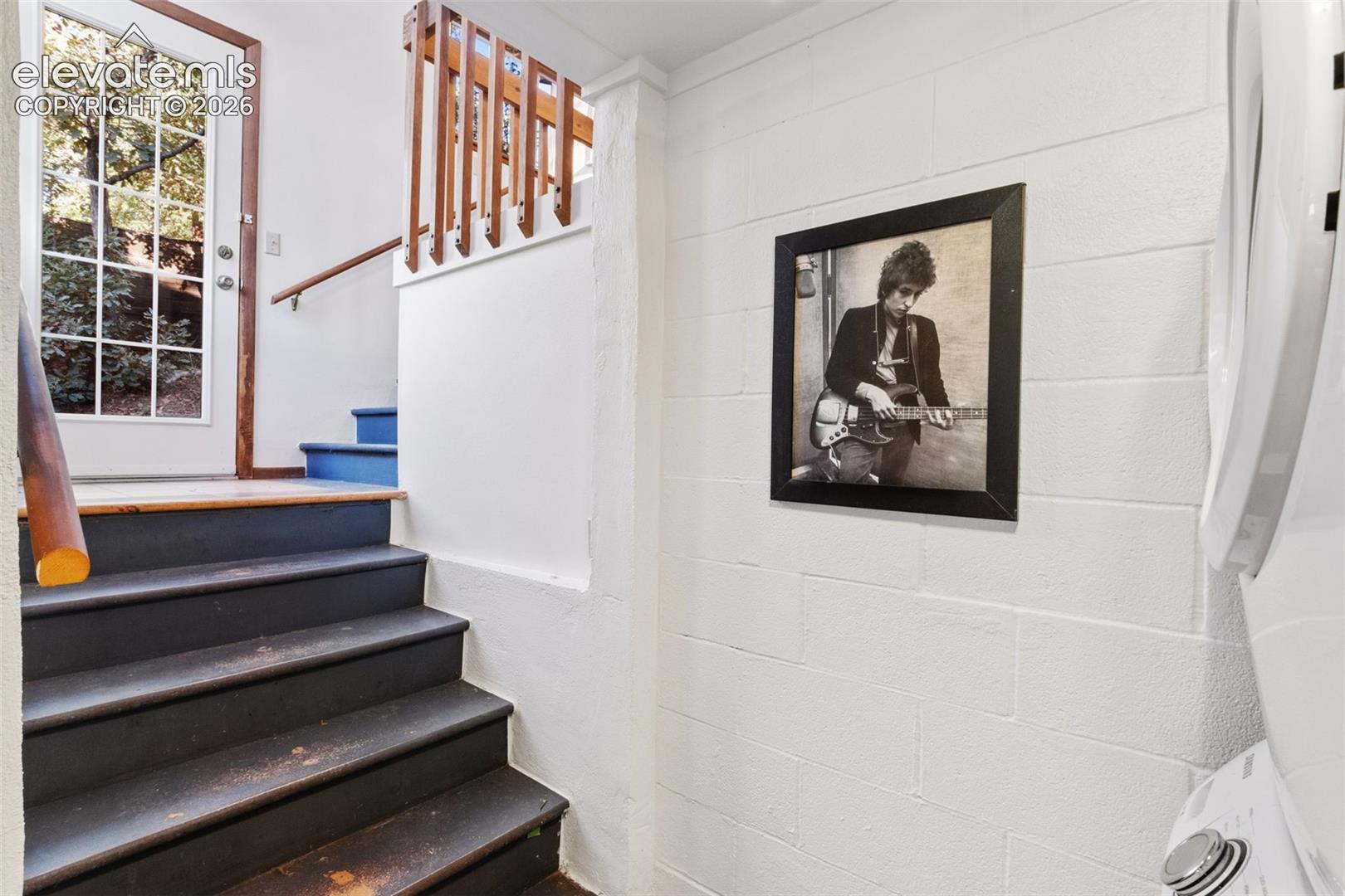 Staircase with dark-finished treads and white painted walls, accented by wooden handrails and a transom window providing natural light