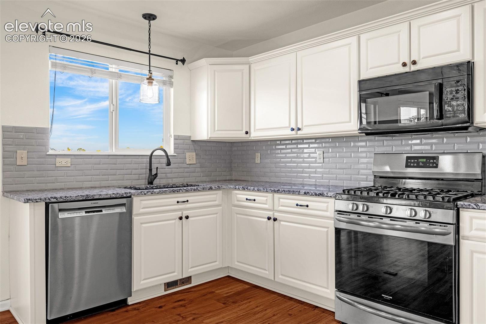 Kitchen featuring white shaker-style cabinetry, grey subway tile backsplash, patterned stone countertops, stainless steel appliances, and wood-finish flooring