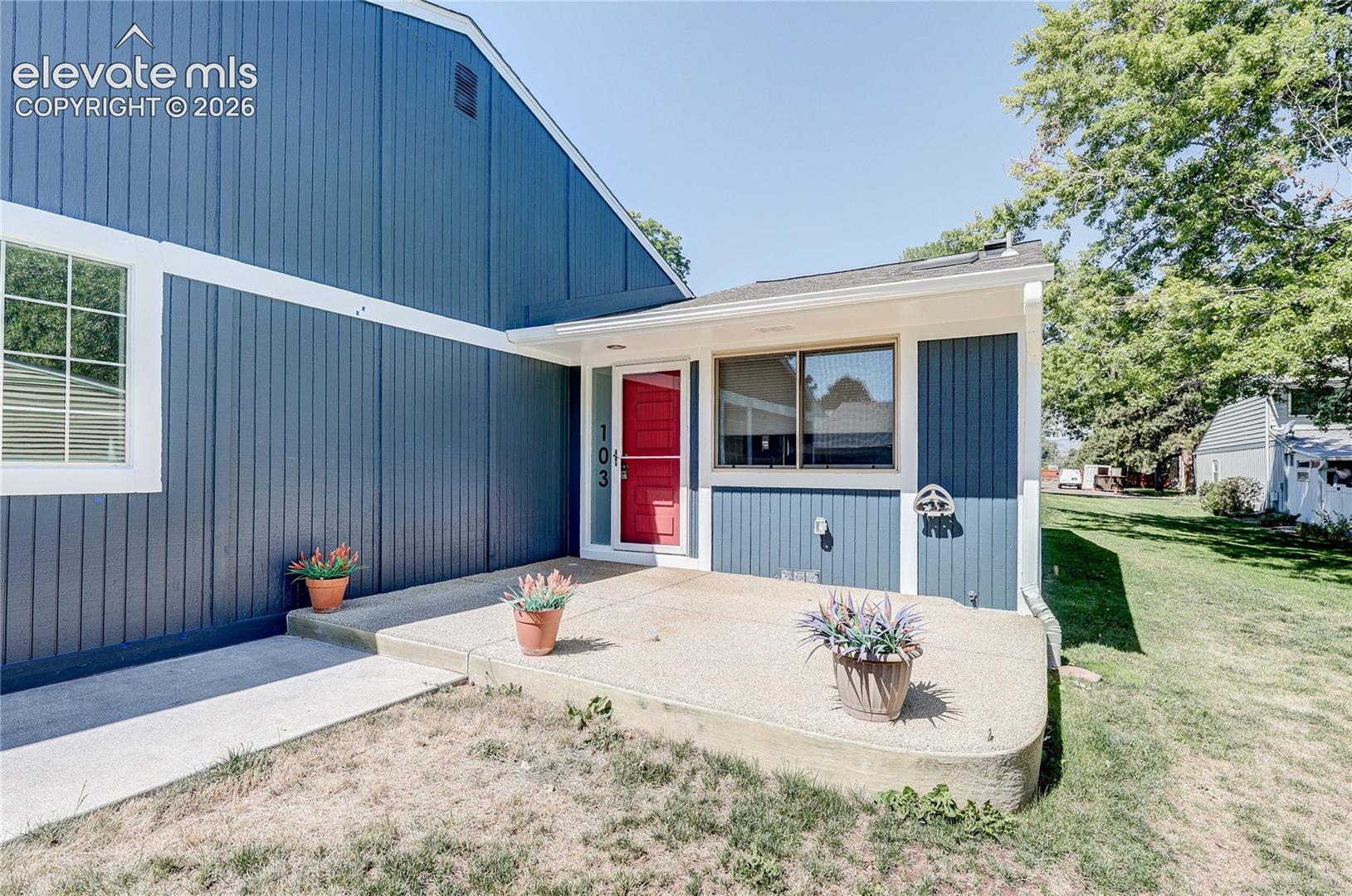 Blue vertical siding exterior featuring a concrete entry porch, contrasting window trim, and a red front door