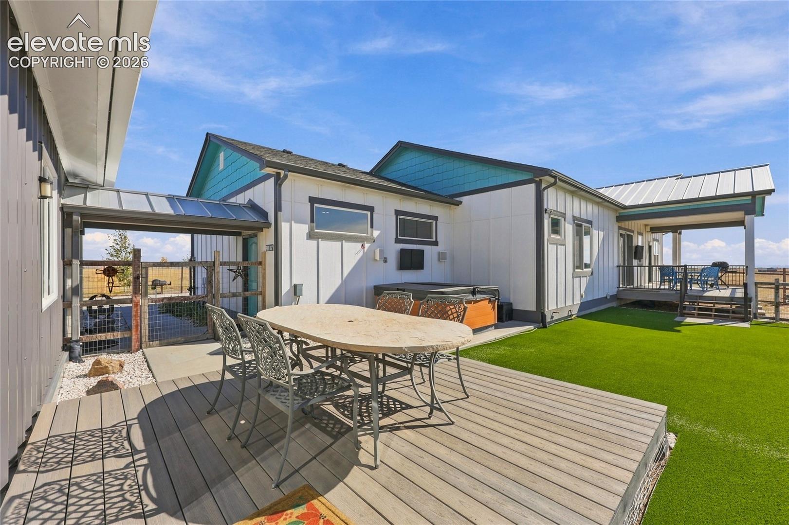 Multi-structure exterior featuring vertical board-and-batten siding, composite decking, synthetic turf lawn, metal roofing, and integrated covered porch spaces