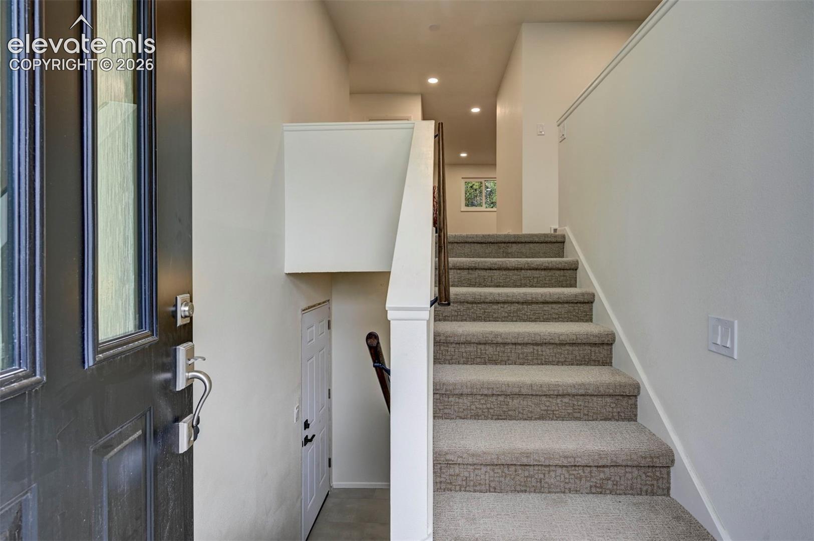 Entryway featuring a dark-toned door with glass paneling, carpeted staircase with a white painted railing, and recessed lighting