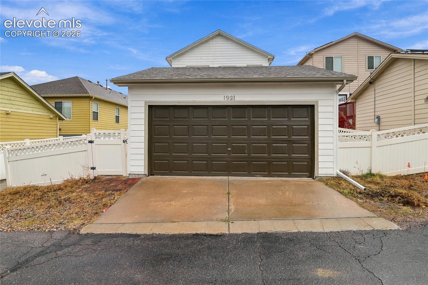 Attached two-car garage with horizontal siding, dual-paneled door, concrete driveway, and white vinyl privacy fencing
