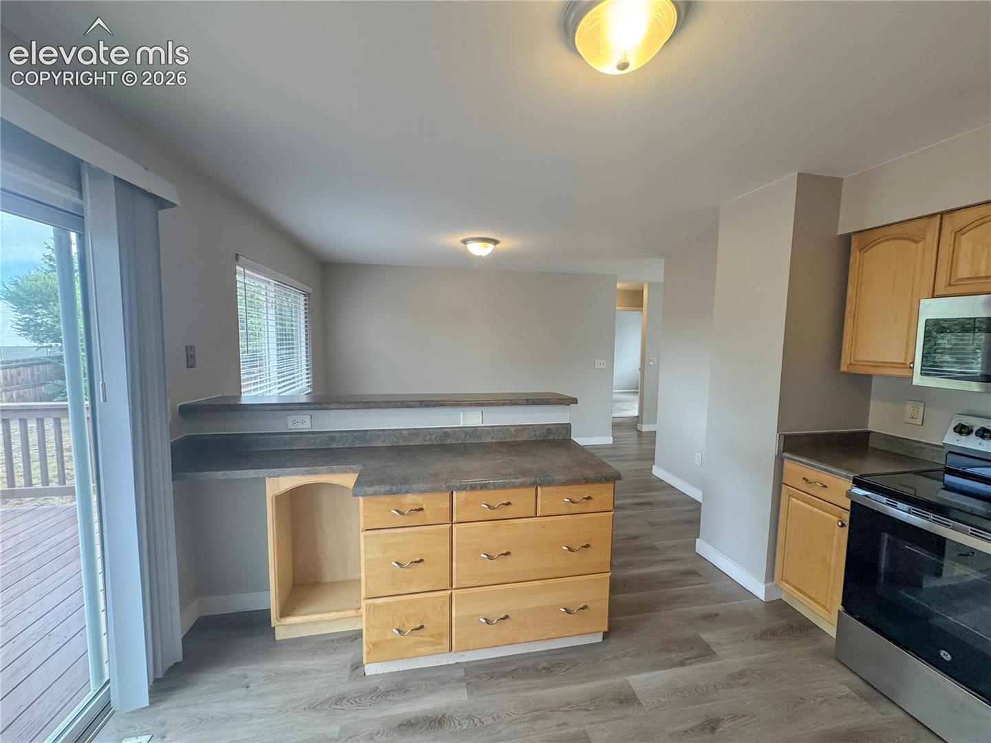 Kitchen featuring a peninsula with solid-surface countertops, light wood-finish cabinetry, stainless steel oven, and wood-finish flooring