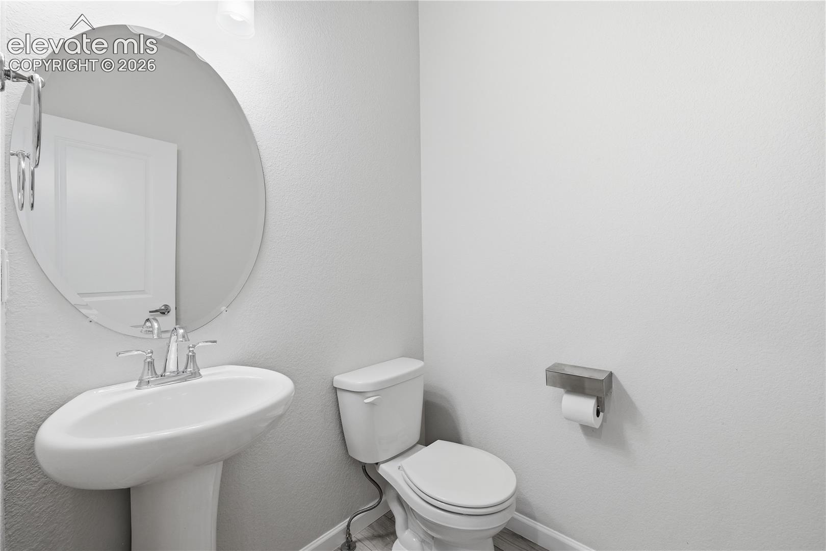 Pedestal sink with chrome faucet, oval mirror, and light gray walls
