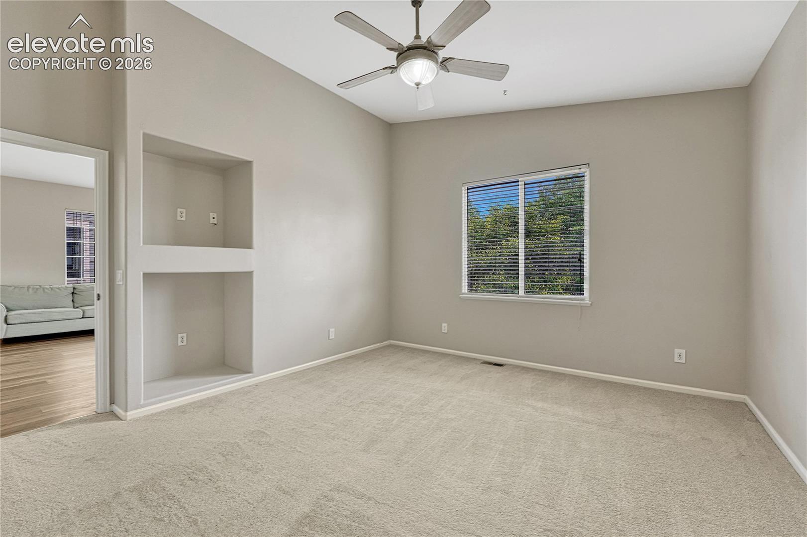 Vaulted ceiling, built-in recessed shelving, neutral wall-to-wall carpeting, and a central ceiling fan with integrated lighting